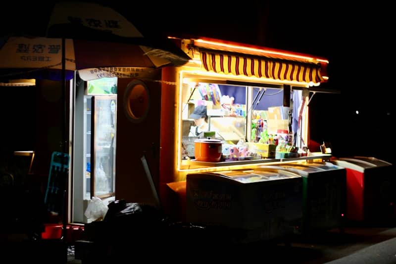A brightly lit food stall operates at night.